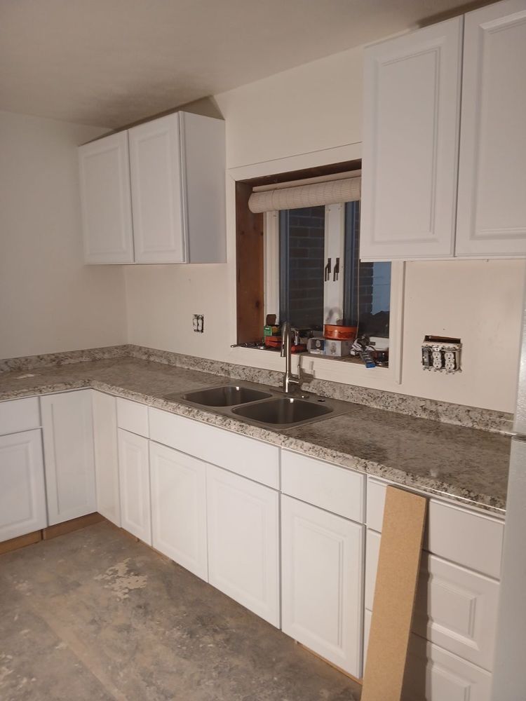 White kitchen with granite countertops, upper and lower cabinets, sink under a window, and unfinished floor area