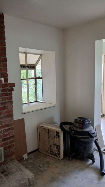 Partially renovated room with window, brick fireplace edge, and vacuum on floor near a crate