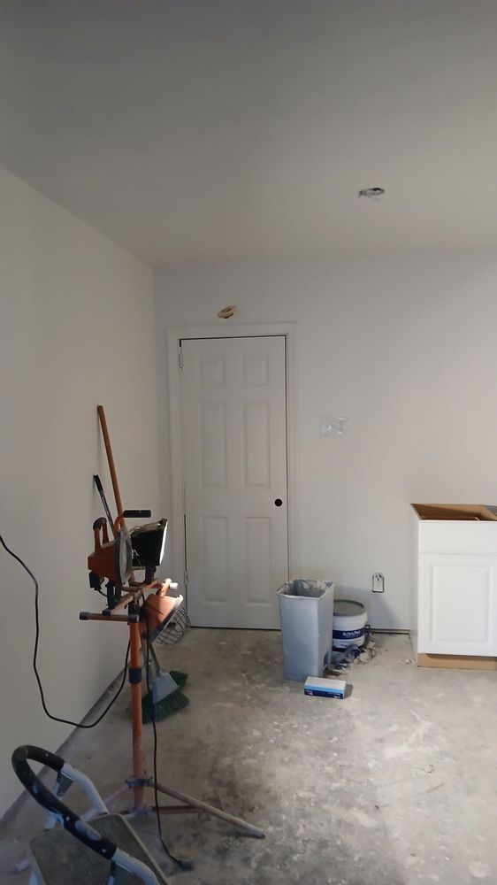Empty room under renovation with tools, paint bucket, and white door against bare walls.