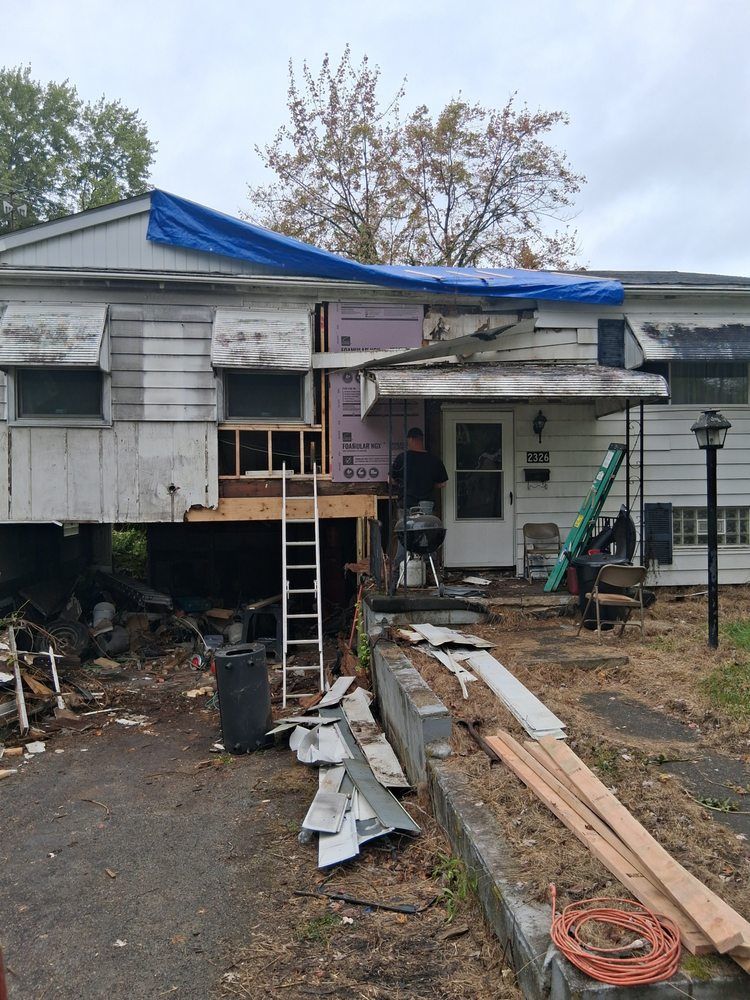 Damaged house with blue tarp roof, ladder, and construction debris in front yard