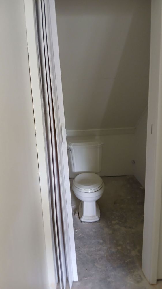 Small empty bathroom with a toilet in a narrow tiled alcove, viewed through a doorway.