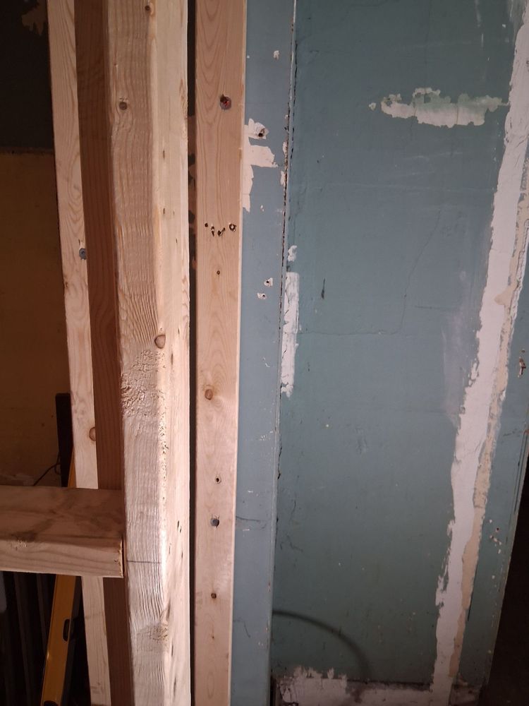 Partially finished interior wall with exposed wood framing and blue drywall patching
