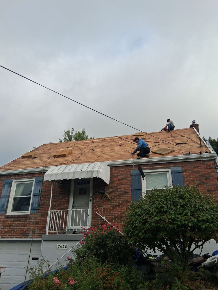 Two workers on a house roof replacing shingles under a gray sky