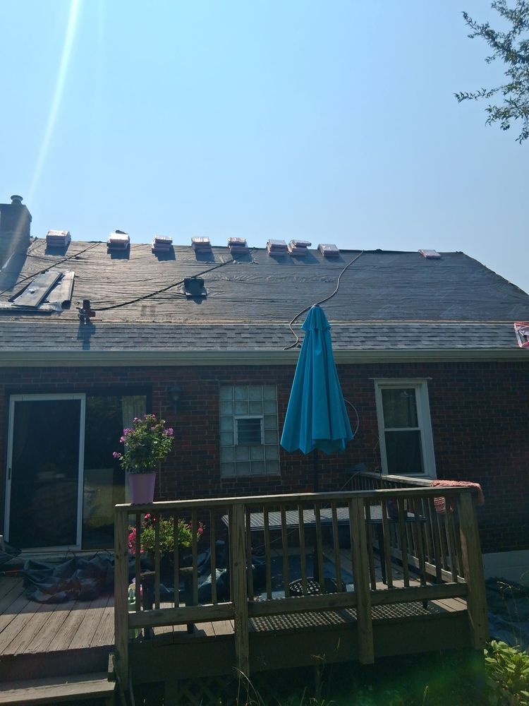 Backyard deck with umbrella, potted flowers, and brick house under bright blue sky