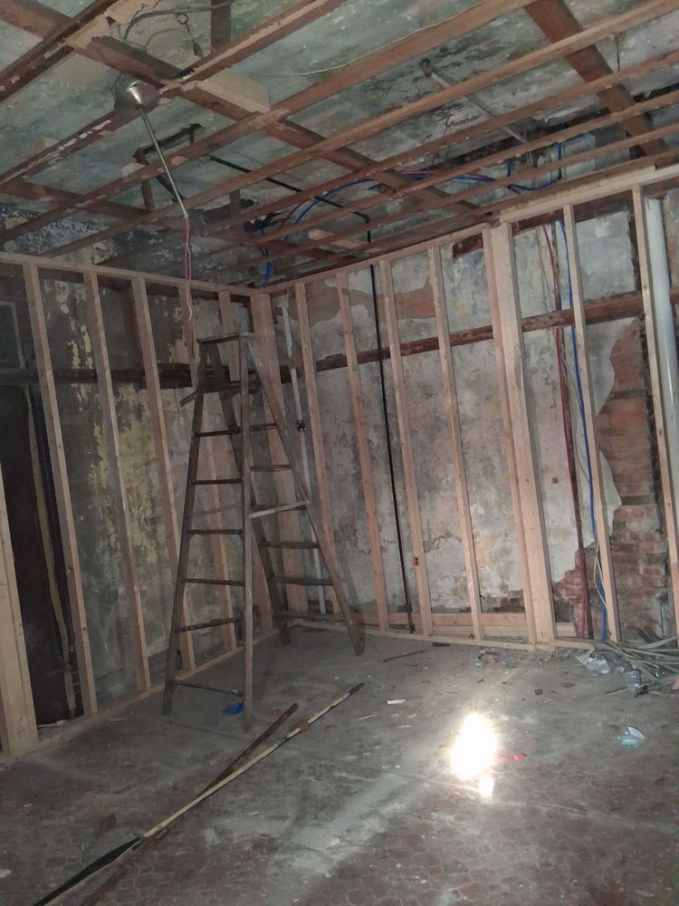 Unfinished room with exposed wall studs, ceiling beams, ladders, and sunlight on the concrete floor
