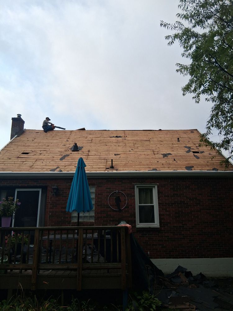House roof under repair with two workers, wooden decking exposed, and a patio umbrella below