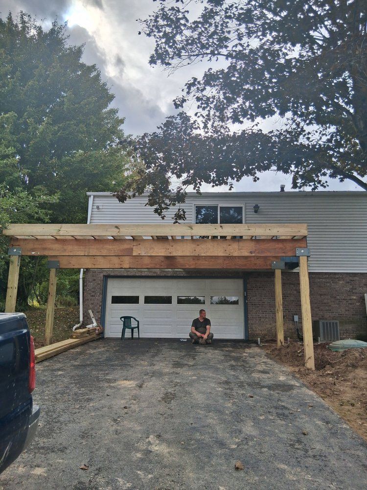 New driveway and wooden carport in front of a gray house, with a person sitting in the garage opening
