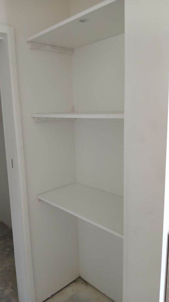 Empty white closet with three shelves and hanging rod.