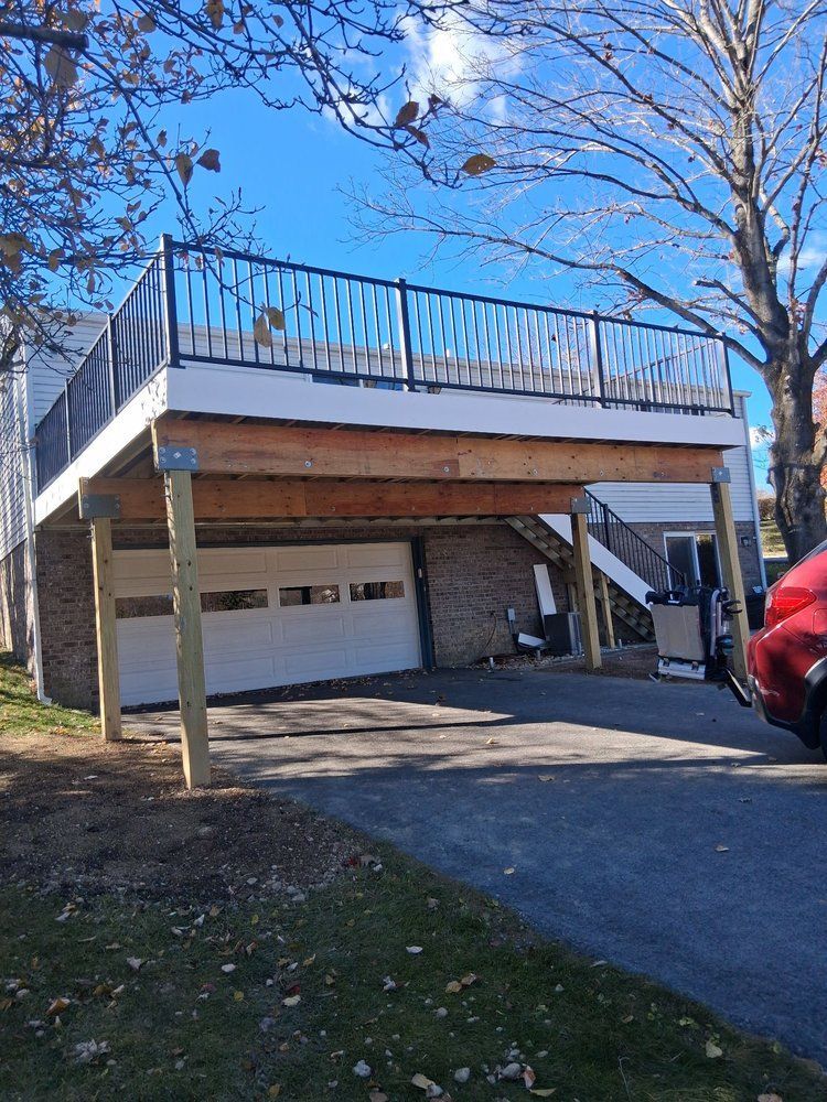 House with elevated deck above a garage, white siding, driveway, and red car under a clear blue sky