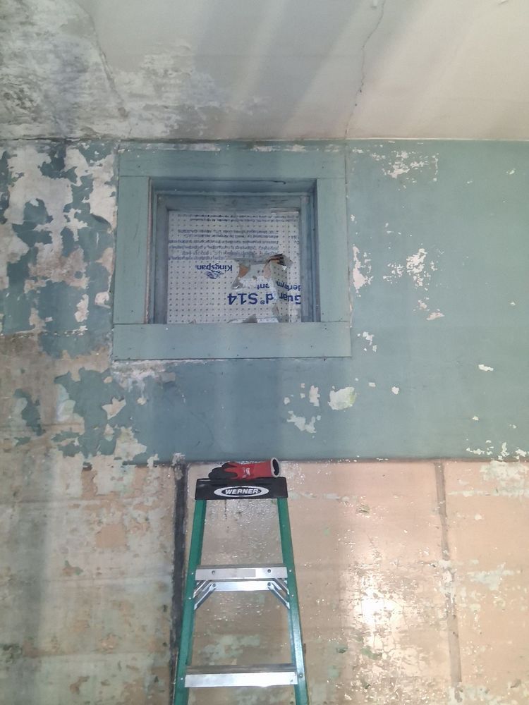 Ladder beneath a small window in a room with peeling blue paint and worn walls