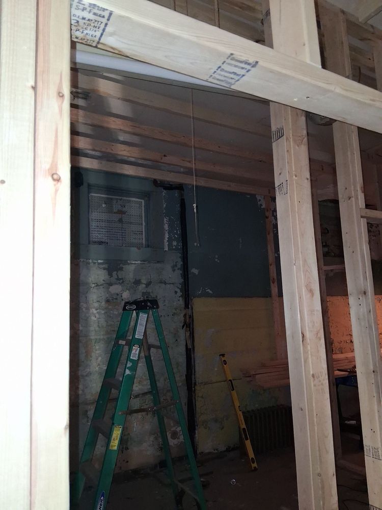 Construction site with unfinished wall framing, a green ladder, and exposed ceiling beams indoors