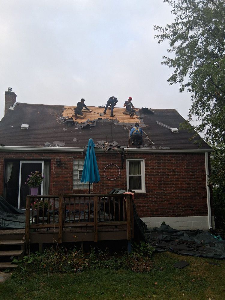 Roofers repairing storm-damaged shingles on a brick house with a deck and blue umbrella