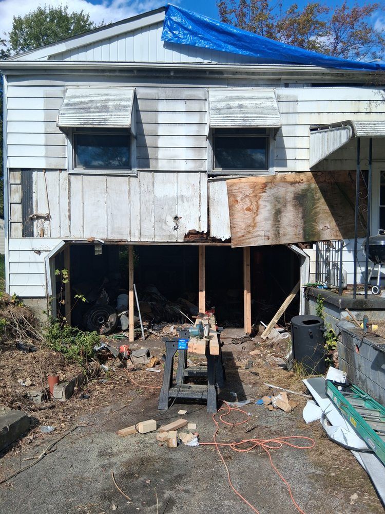 House exterior under repair with exposed lower level, debris, and blue tarp on the roof