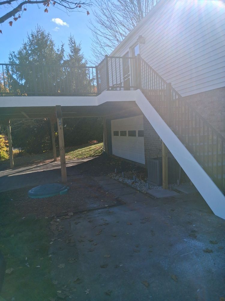 Backyard deck with white stairs, a covered patio, and a driveway in bright sunlight