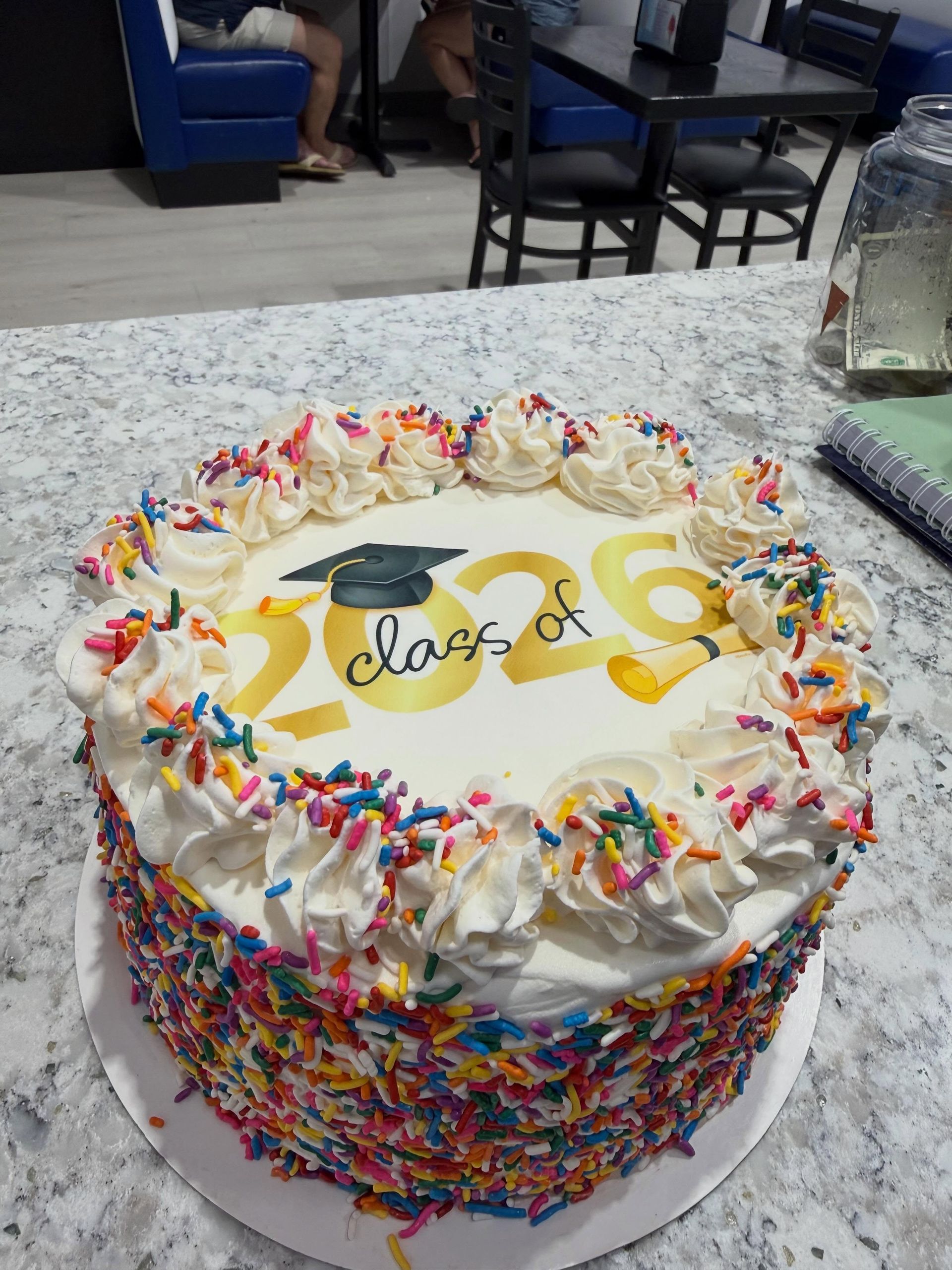 Colorful 20th birthday cake with rainbow sprinkles and piped frosting on a white table.