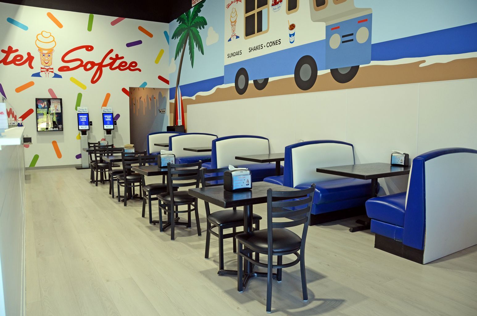 Empty modern café interior with blue booths, black tables, and a colorful beach mural on the wall