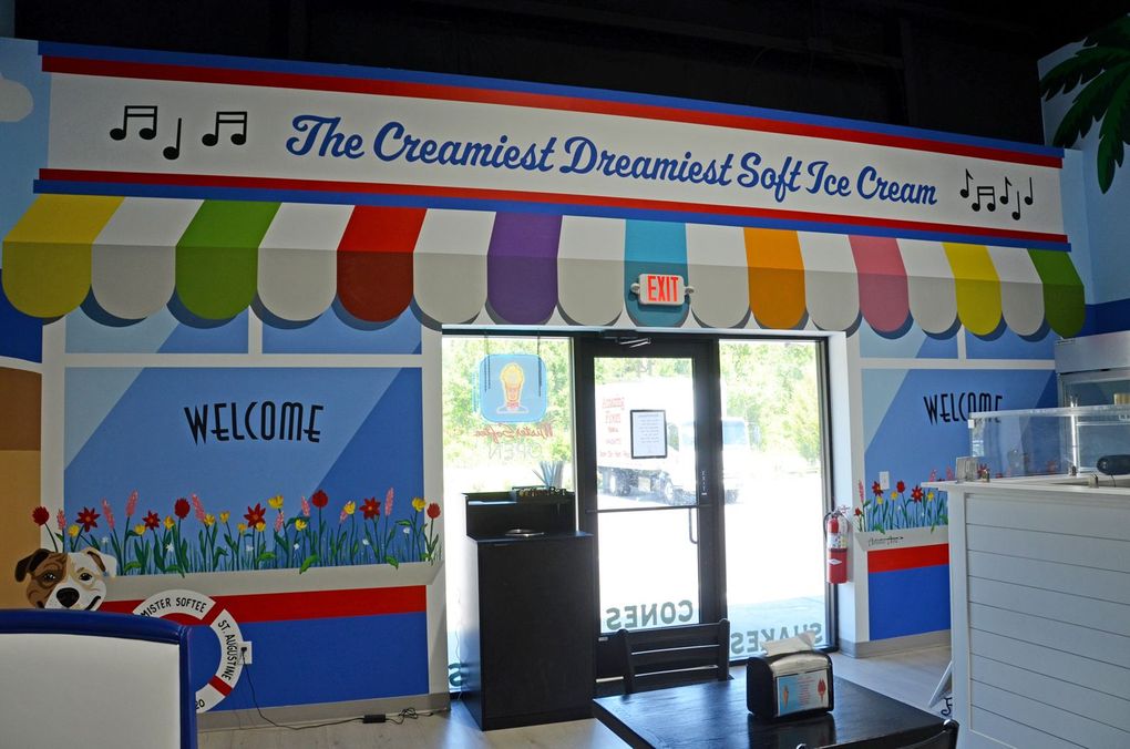 Colorful daycare entrance with rainbow awning, music notes, welcome mural, and glass doors.