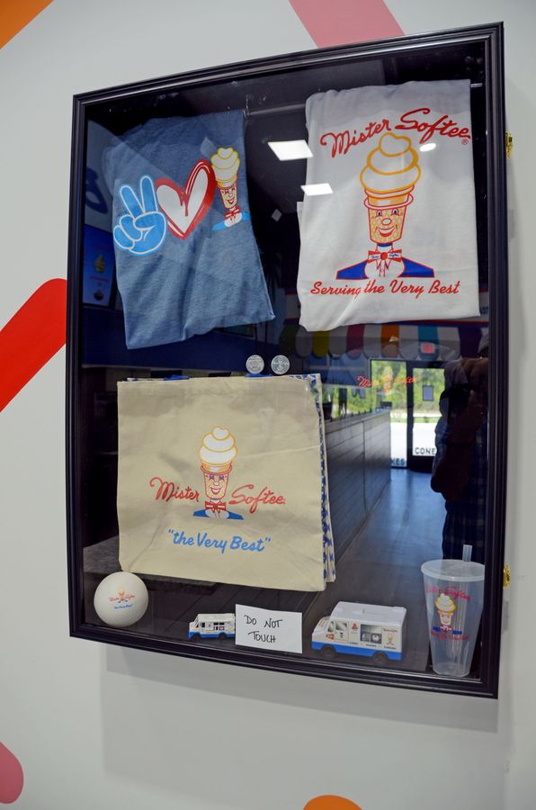 Framed T-shirts and small items displayed in a glass case on a wall.