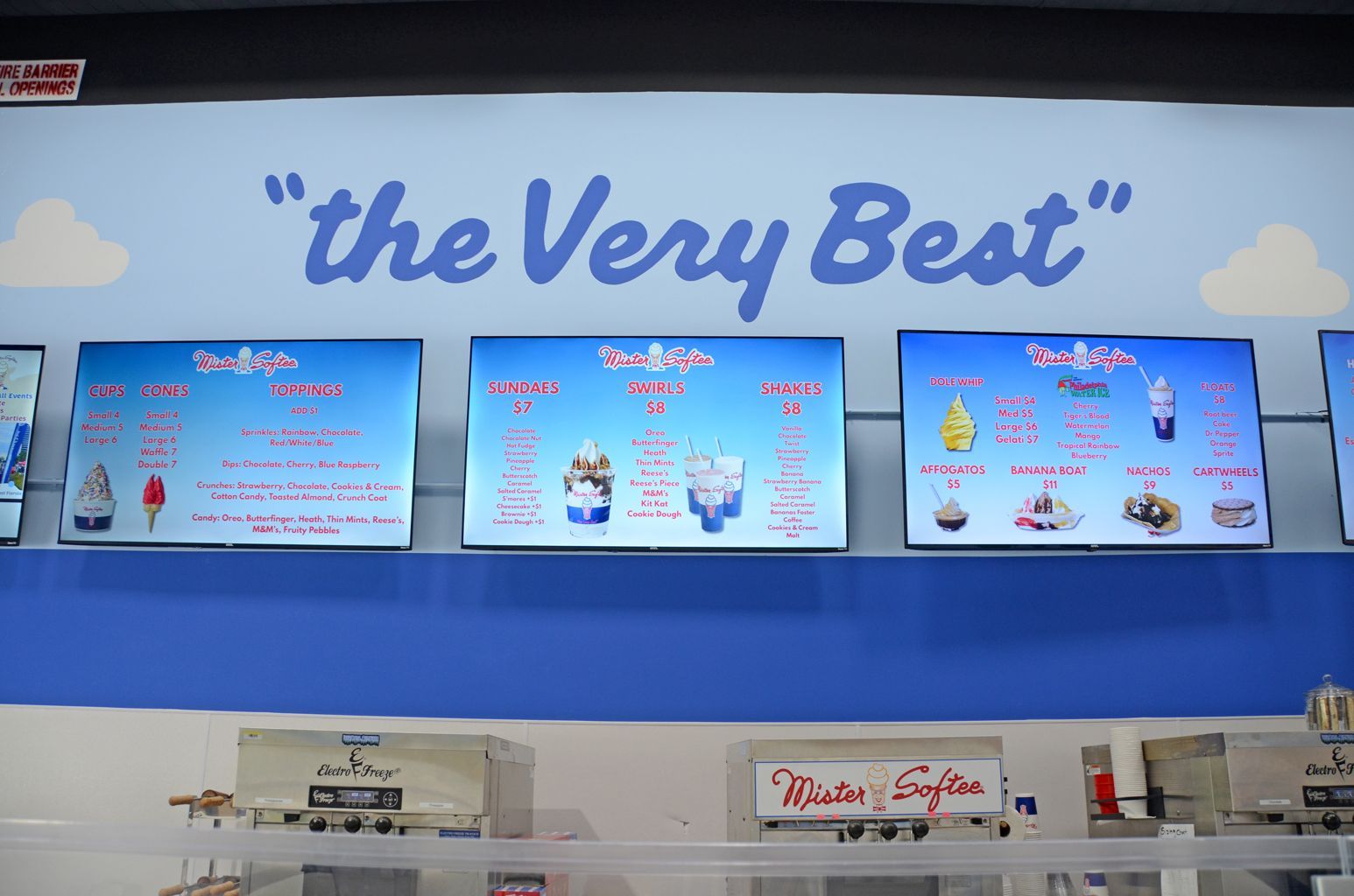 Blue restaurant menu boards under the sign “The Very Best” on a white wall.