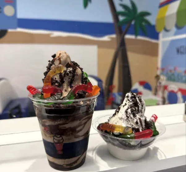 Two ice cream sundaes topped with whipped cream and cherries on a counter