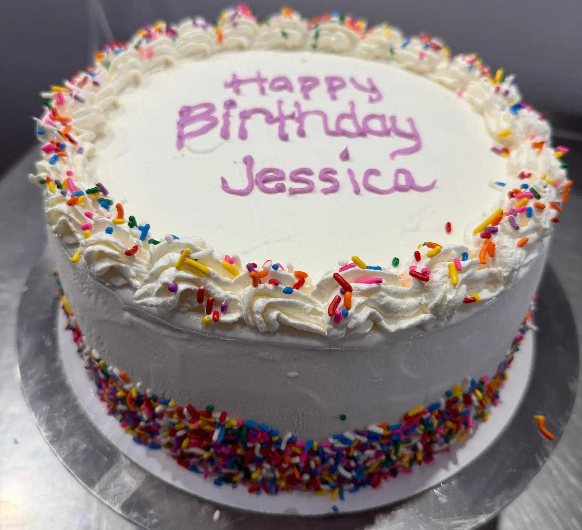 White frosted birthday cake with rainbow sprinkles and “Happy Birthday Jessica” written on top