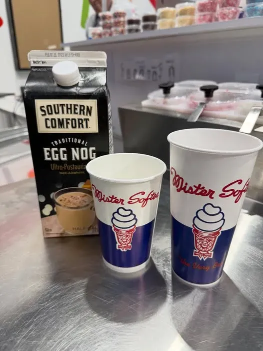 Two Krispy Kreme cups beside a Southern Comfort egg nog carton on a store counter