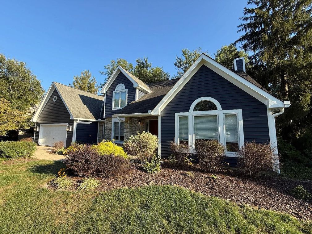 Suburban house with dark gray siding, white trim, and landscaped front yard on a sunny day