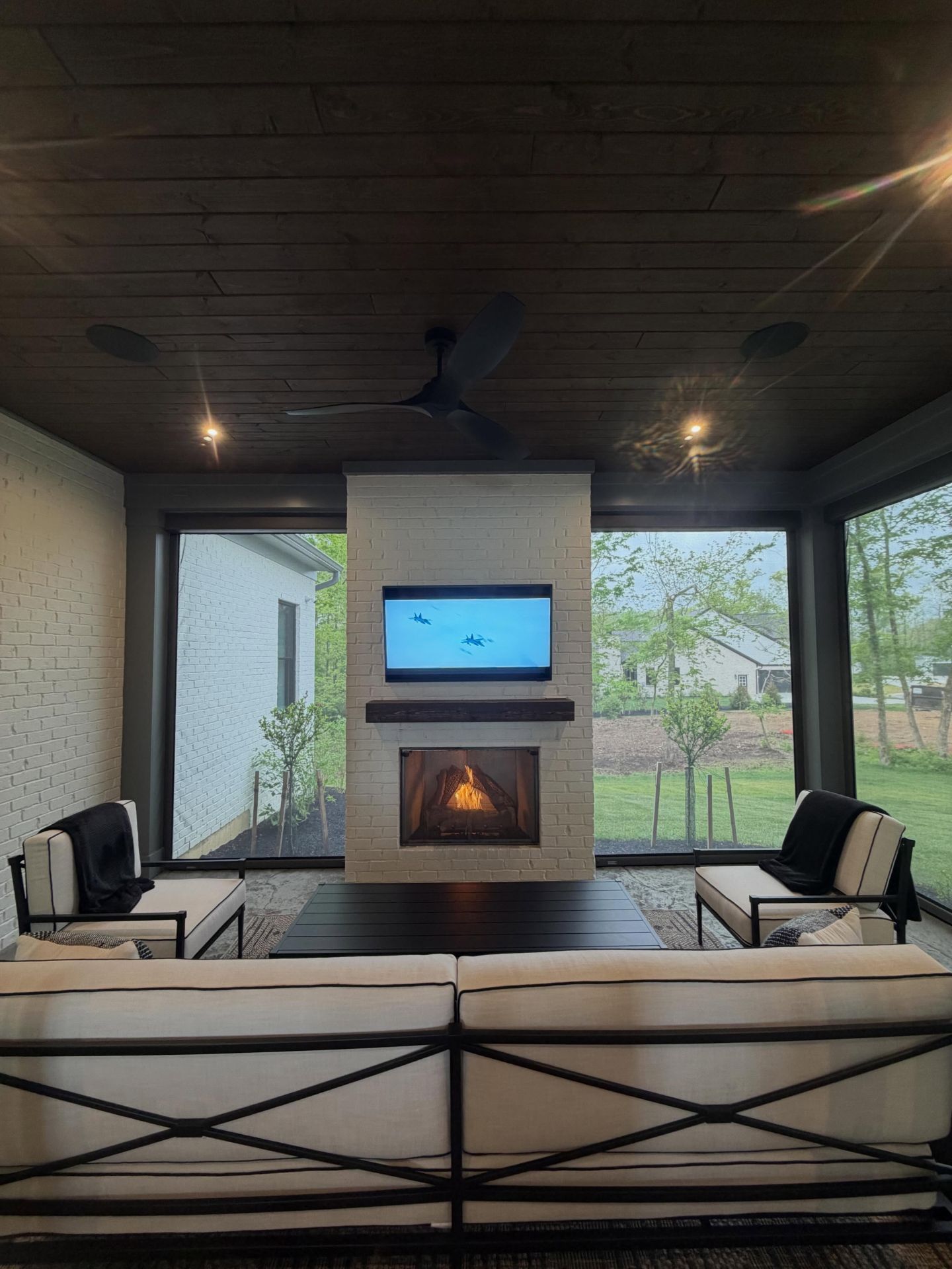 Covered patio with fireplace, wall-mounted TV, and lounge seating overlooking a yard