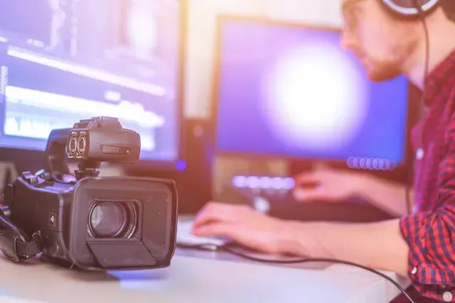 A man is sitting at a desk with a camera and a computer.