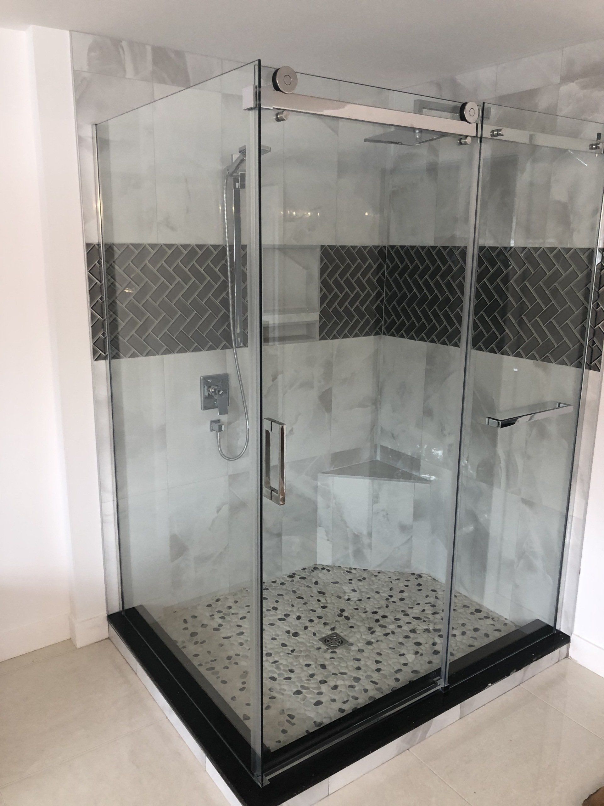 Cabine de douche en verre avec accents de carrelage noir et gris et sol en pierre.
