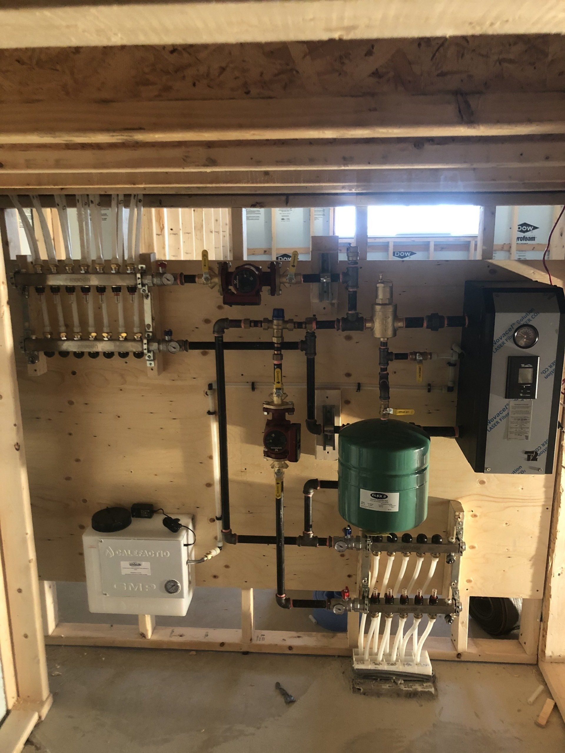 Système de plomberie avec tuyaux, réservoirs et panneau de commande, monté sur un mur en bois dans un contexte de construction.