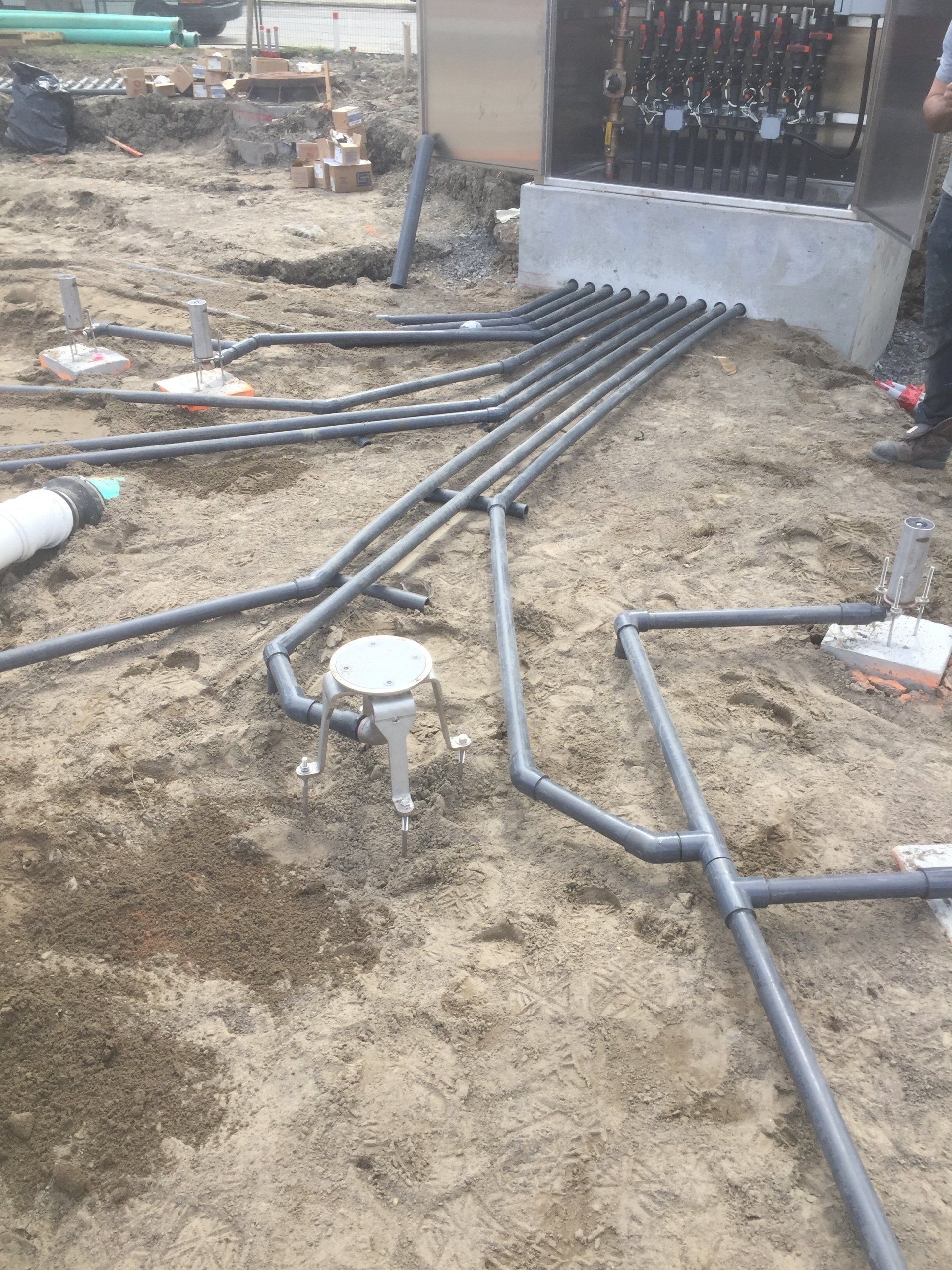 Tuyaux en PVC gris posés sur un sol en terre battue, reliés à une structure en blocs de béton ; chantier de construction.