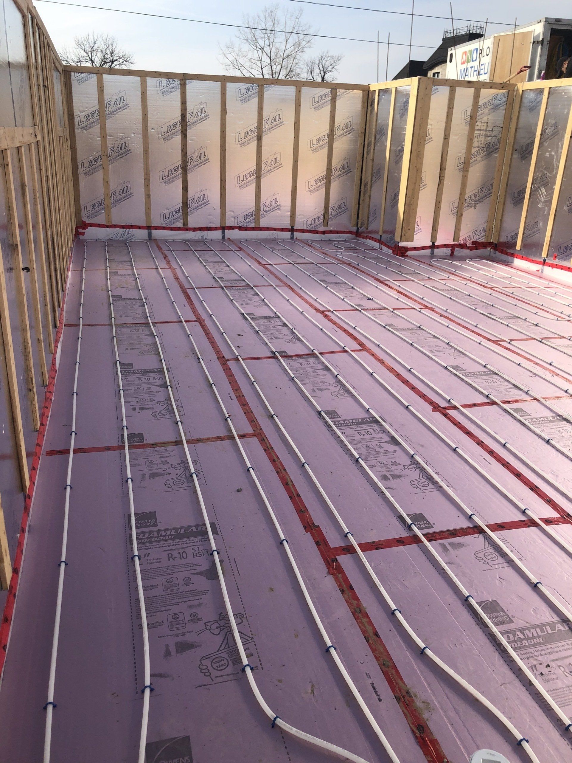 Intérieur d'une pièce en construction avec isolation rose, tubes de chauffage radiant et ossature en bois.