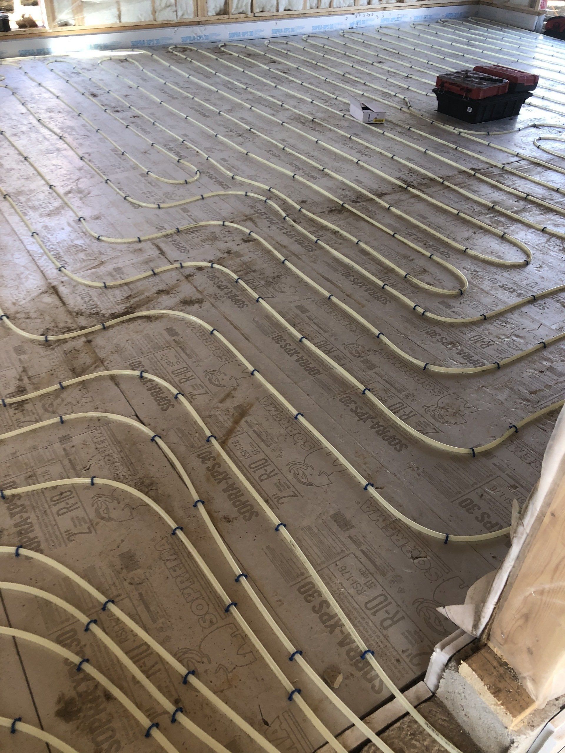 Des tubes jaunes disposés en grille sur un sol en béton, probablement pour un système de chauffage radiant, dans un contexte de construction.