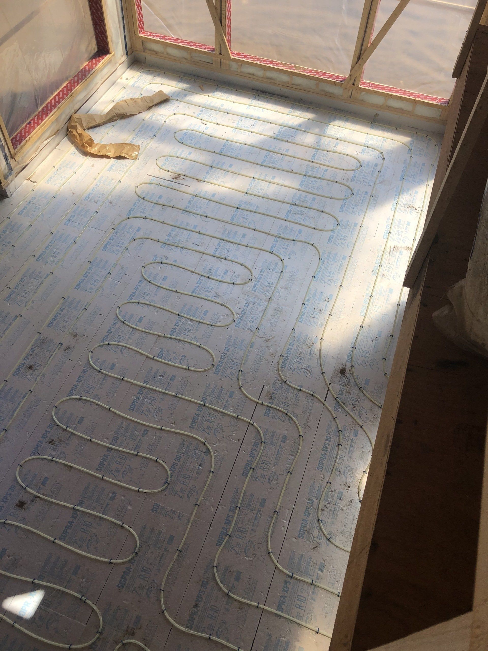 Vue intérieure d'une petite structure avec un sol bleu et un système de tuyaux en serpentin, probablement pour le chauffage radiant.