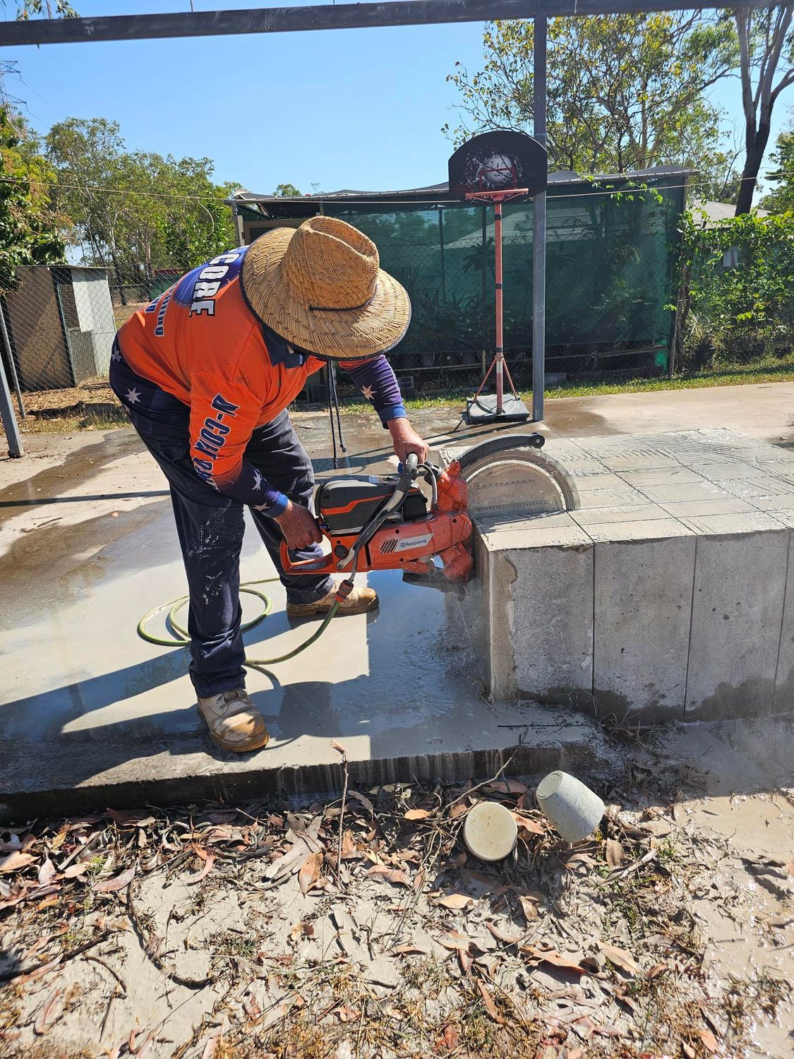A worker in orange shirt cuts concrete block with a saw outdoors  — Di-Core Drilling and Cutting in Darwin, NT