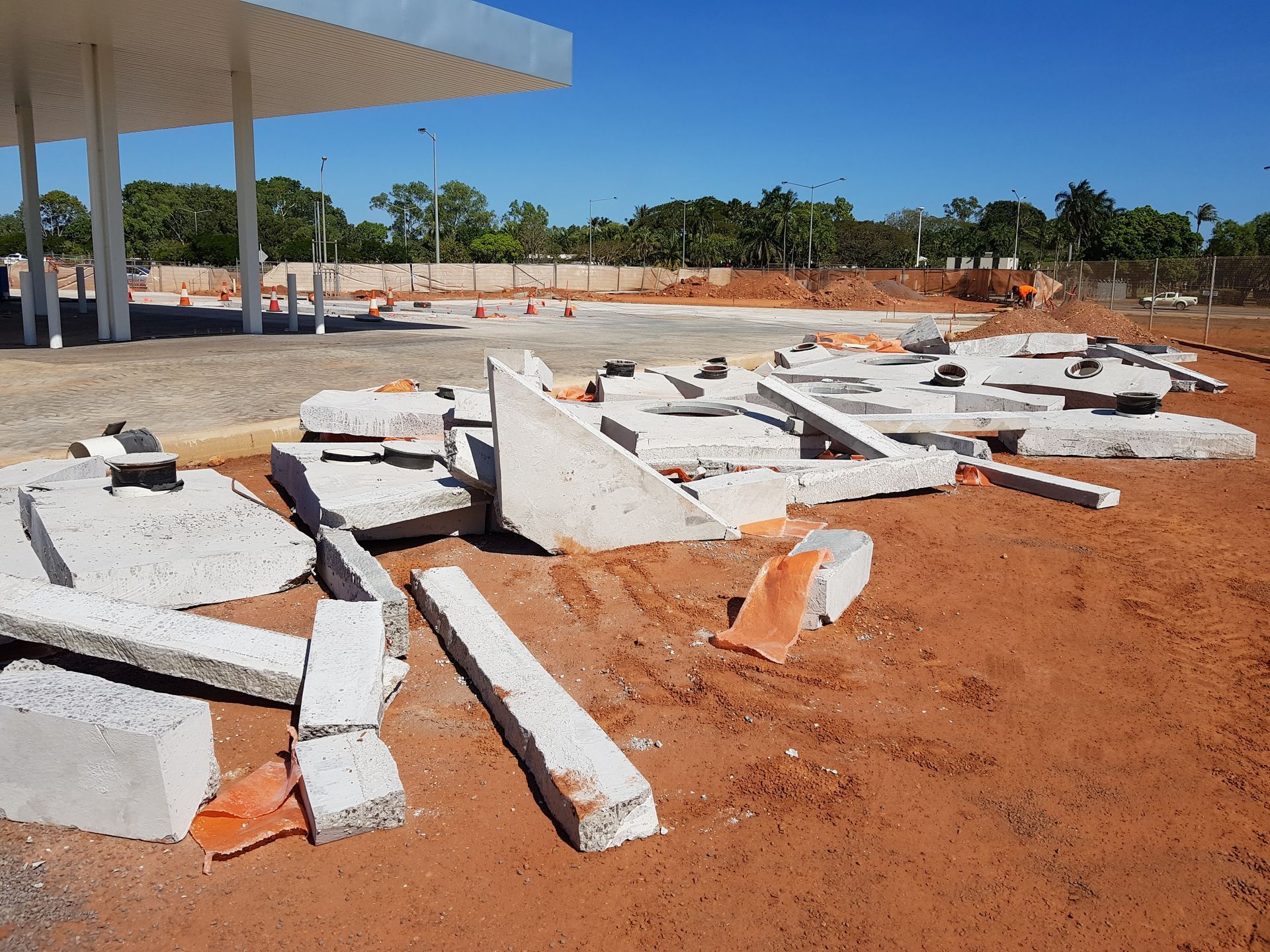 Broken concrete pieces scattered on red dirt at a gas station, with a white canopy overhead.