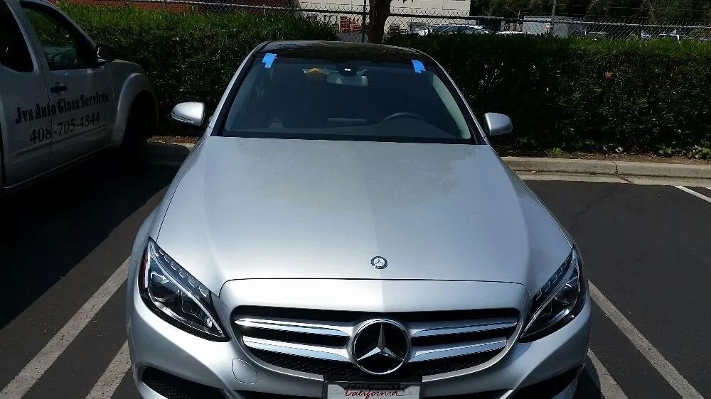 Silver Mercedes-Benz sedan parked in a lot. The windshield has blue tape.
