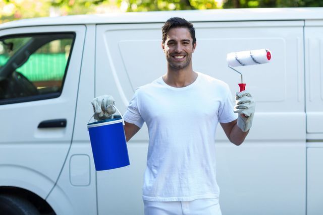 Painter with paint roller and bucket stands in front of a white van.