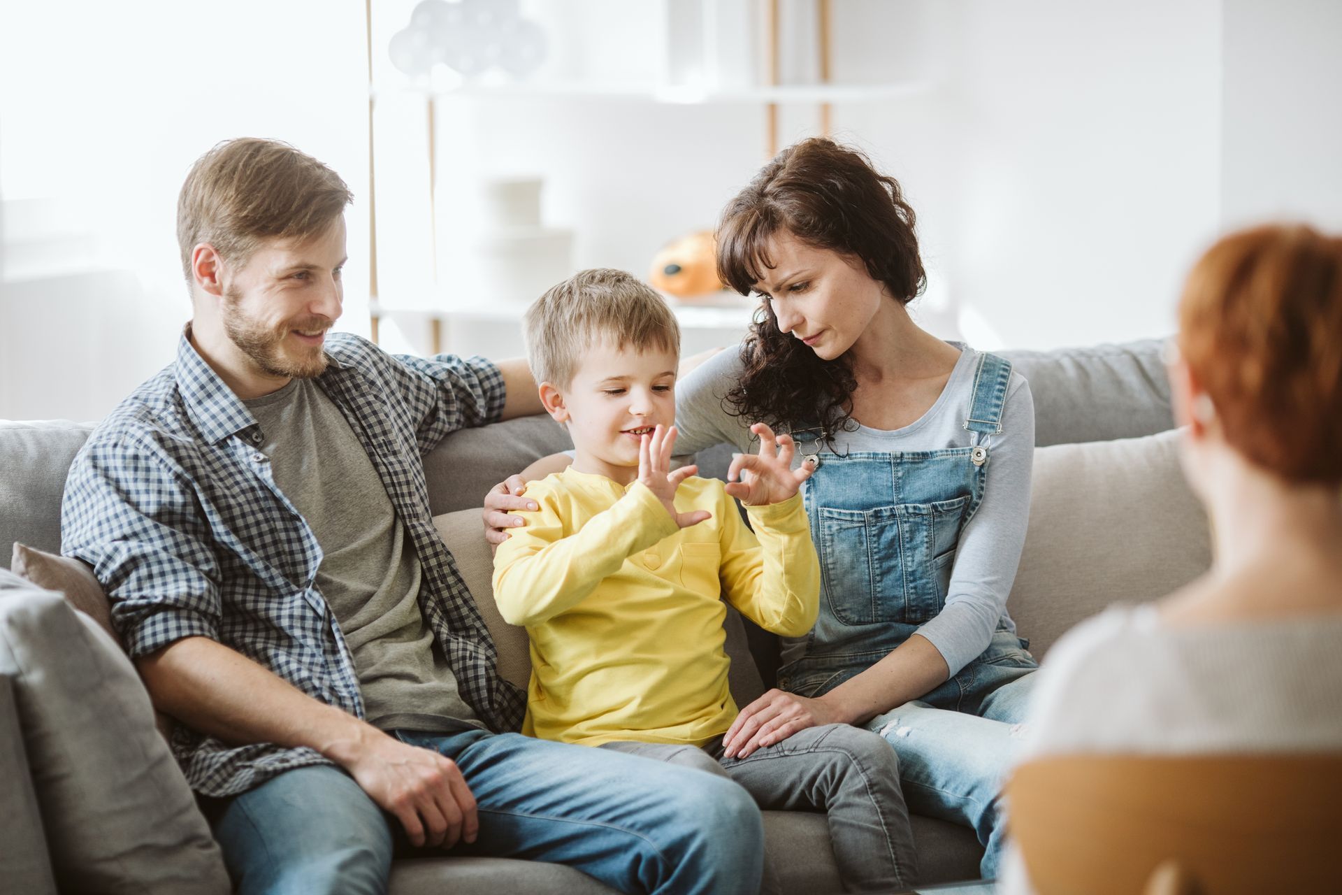 Family sitting on a couch, child holding a yellow toy while adults smile in a bright living room