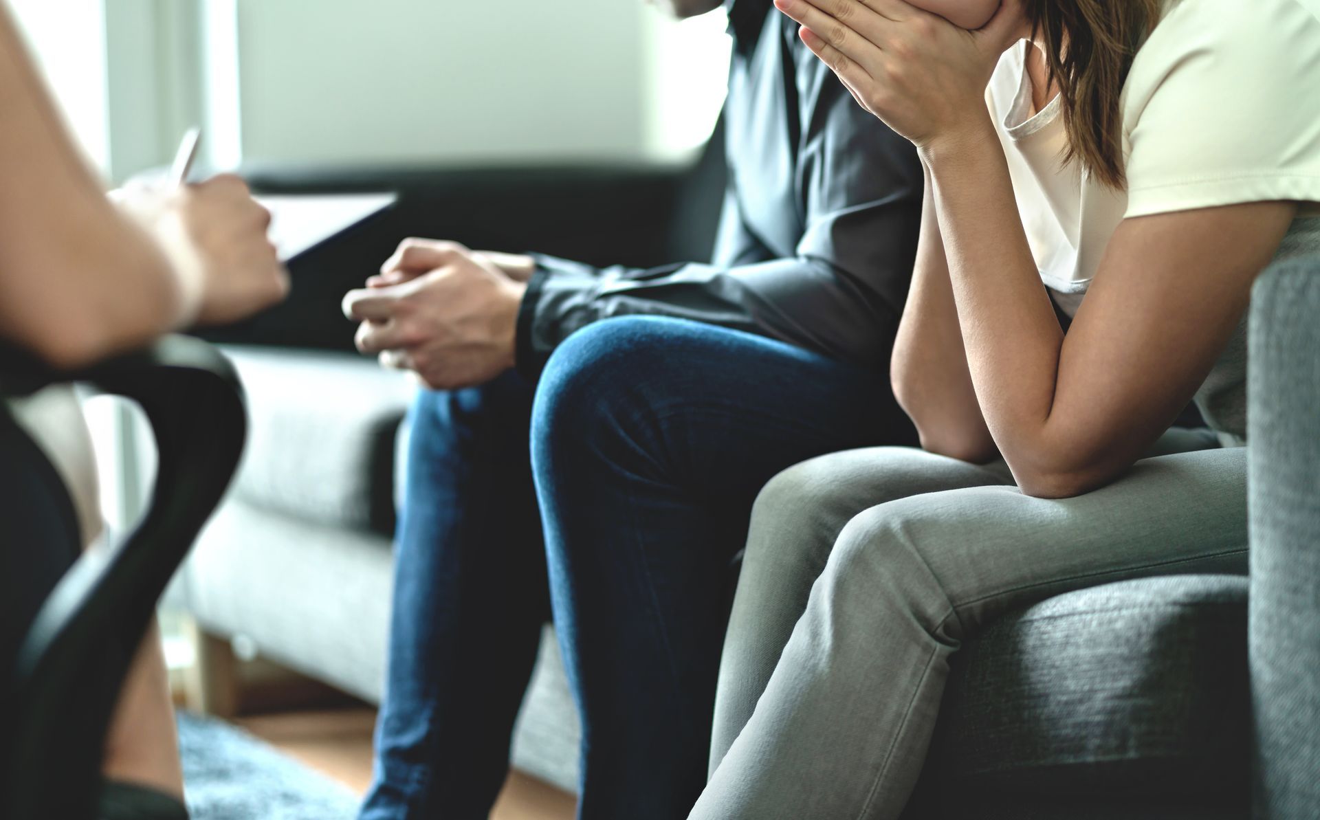 People seated on a couch in a counseling session, one speaking with hands clasped, another listening attentively.