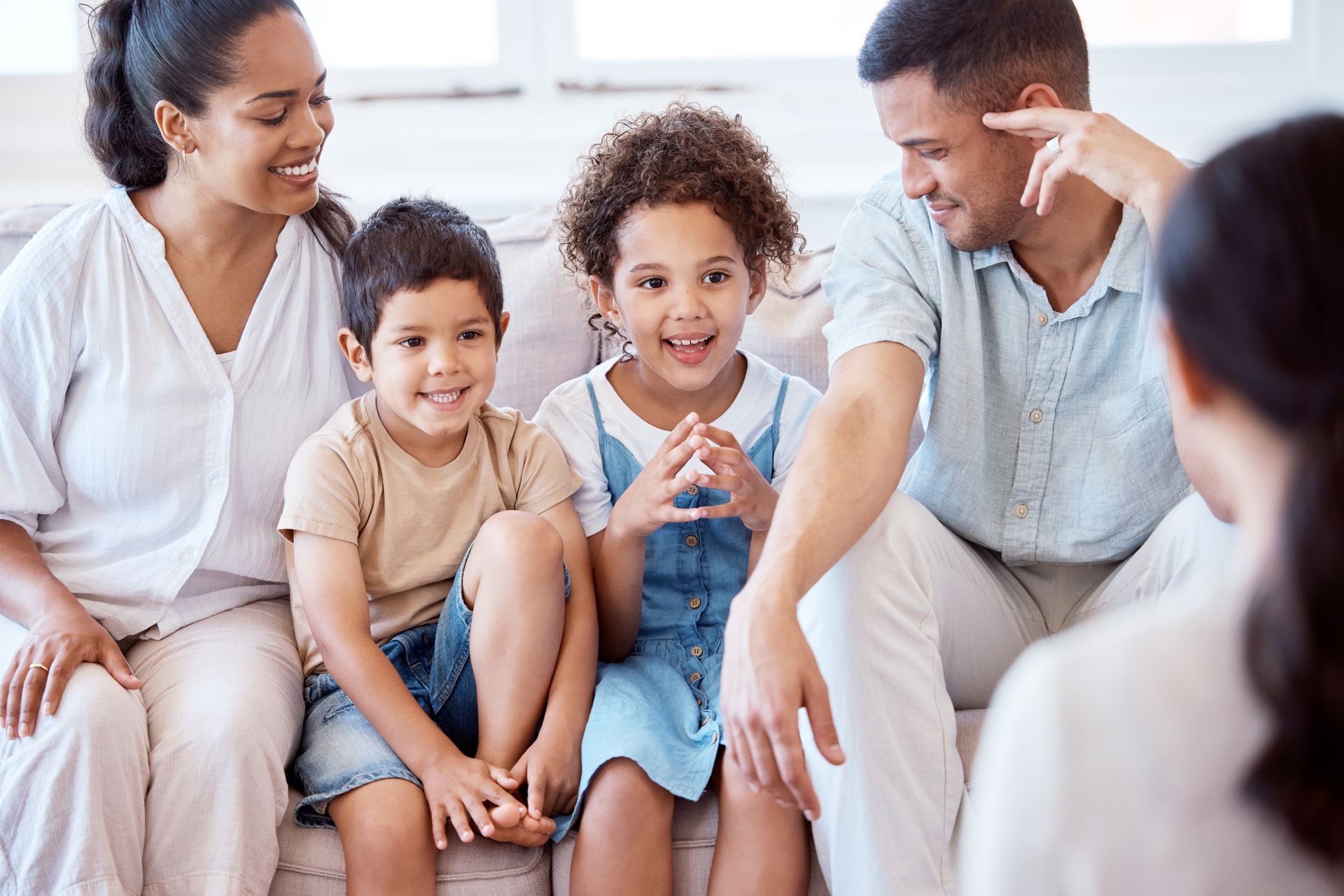 Family sitting on a couch, smiling and talking together in a bright living room.