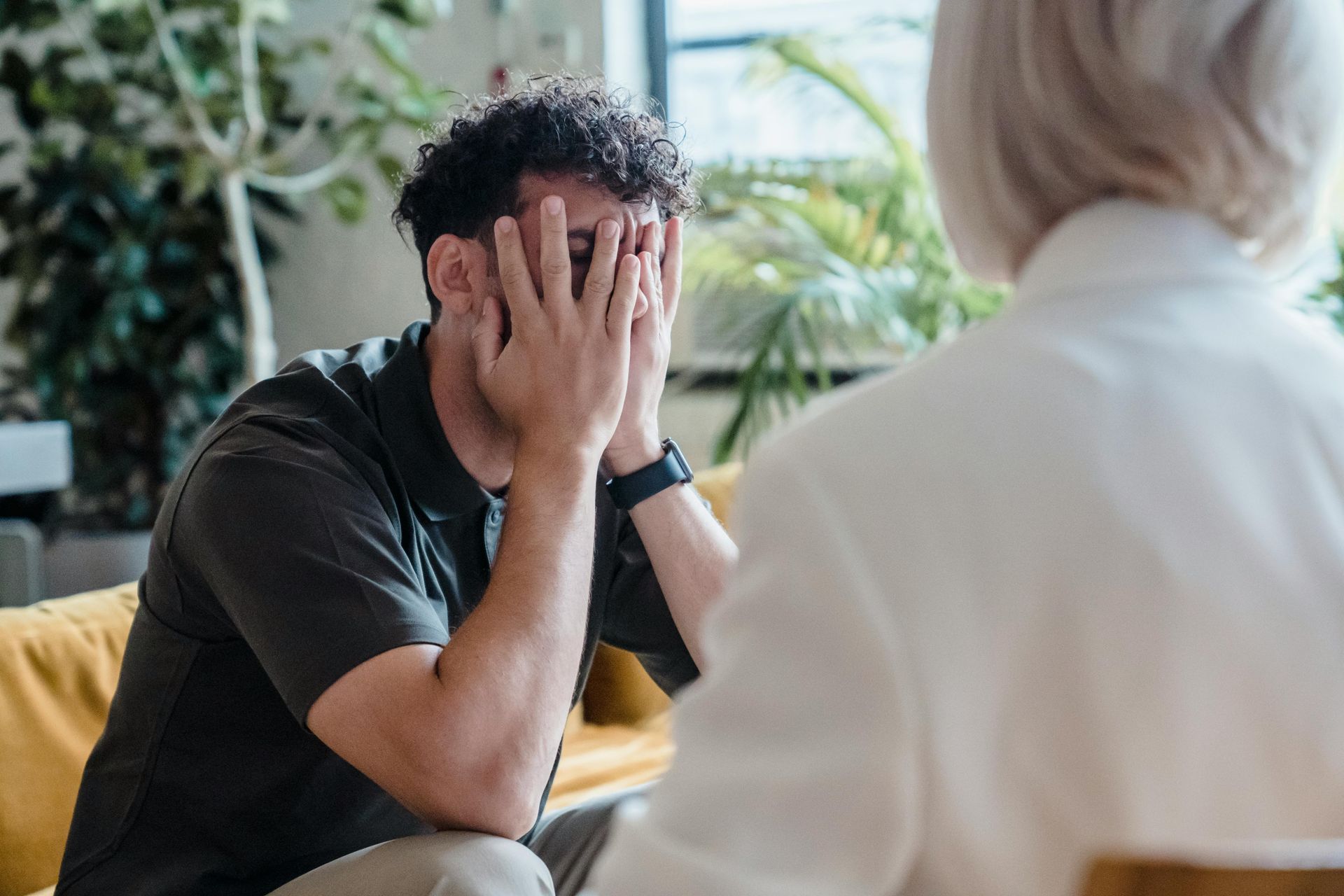 A man is covering his face with his hands while talking to a woman.