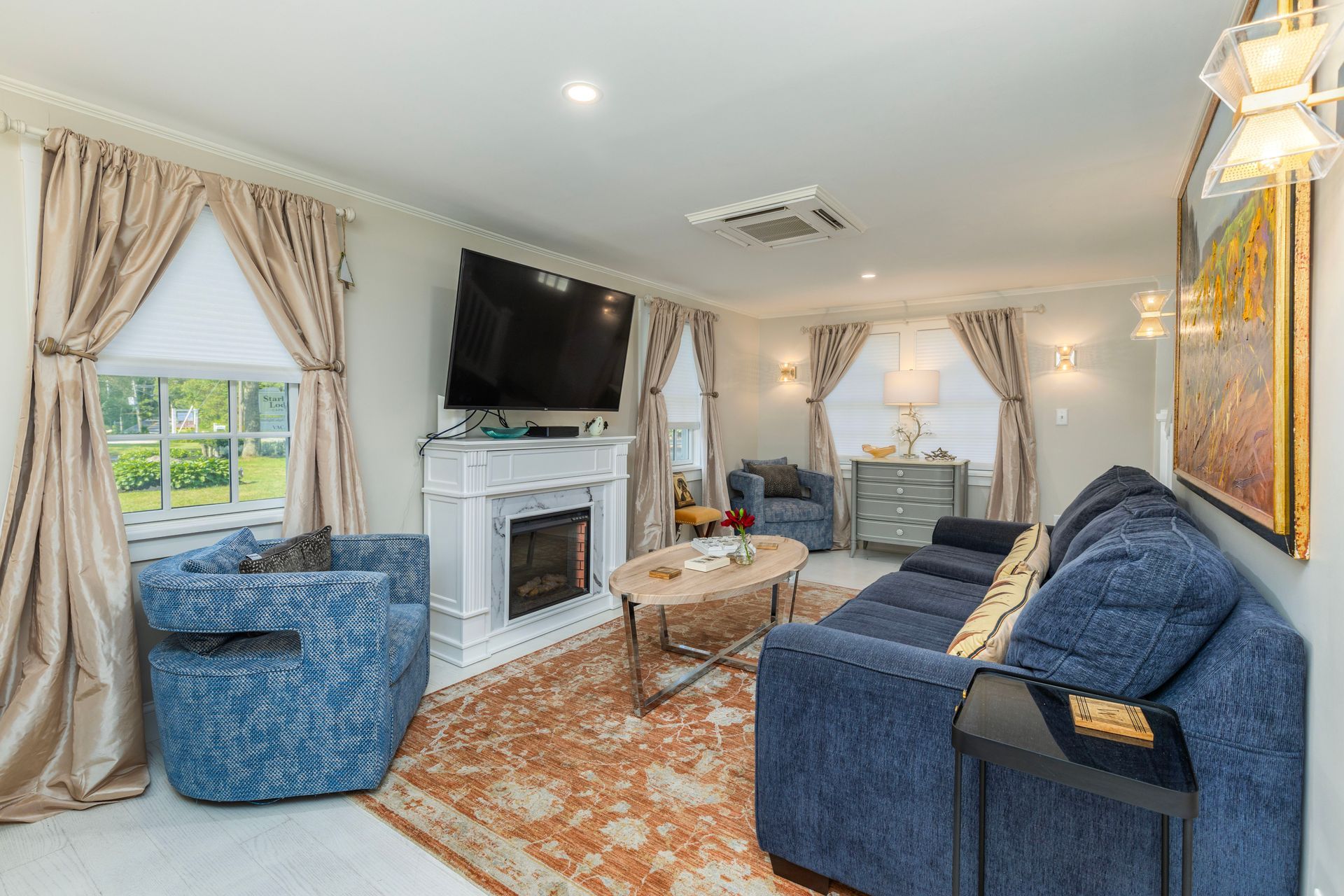 Cozy living room with blue furniture, fireplace, gold curtains, and a patterned rug.