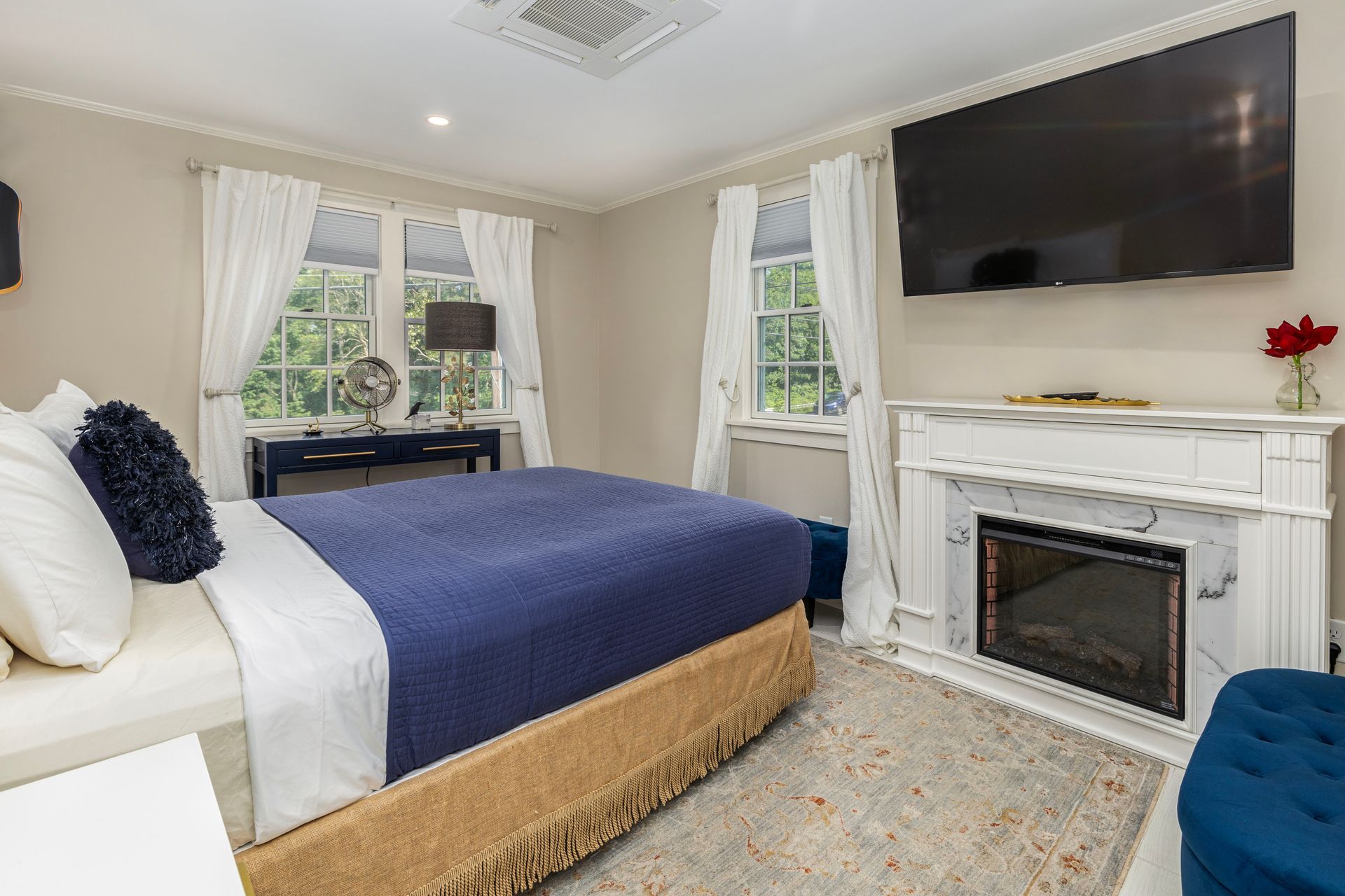 Bedroom with bed, fireplace, TV, windows, blue and white decor.