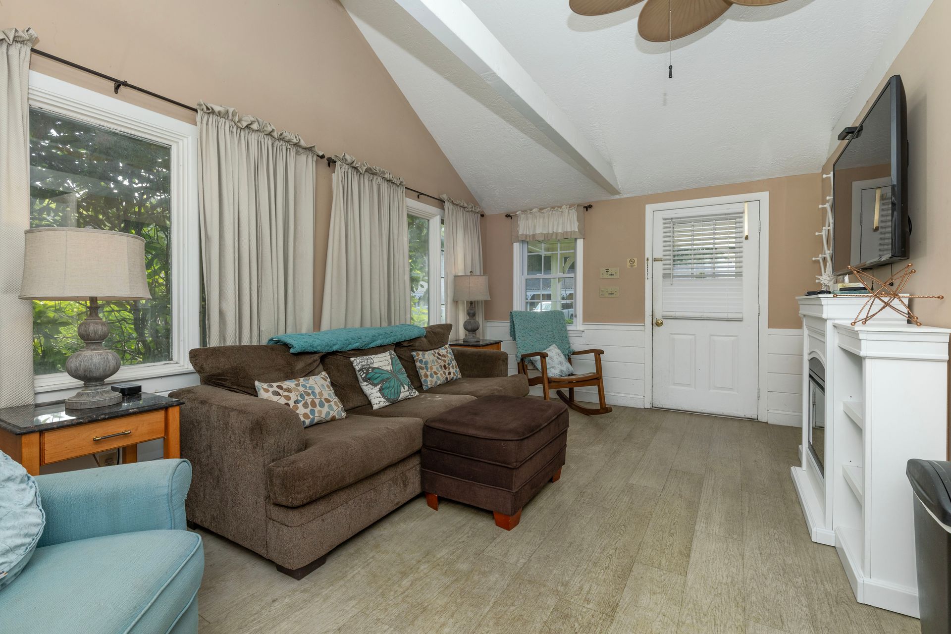 Living room with brown couch, ottoman, and blue armchair, with windows and a white fireplace.
