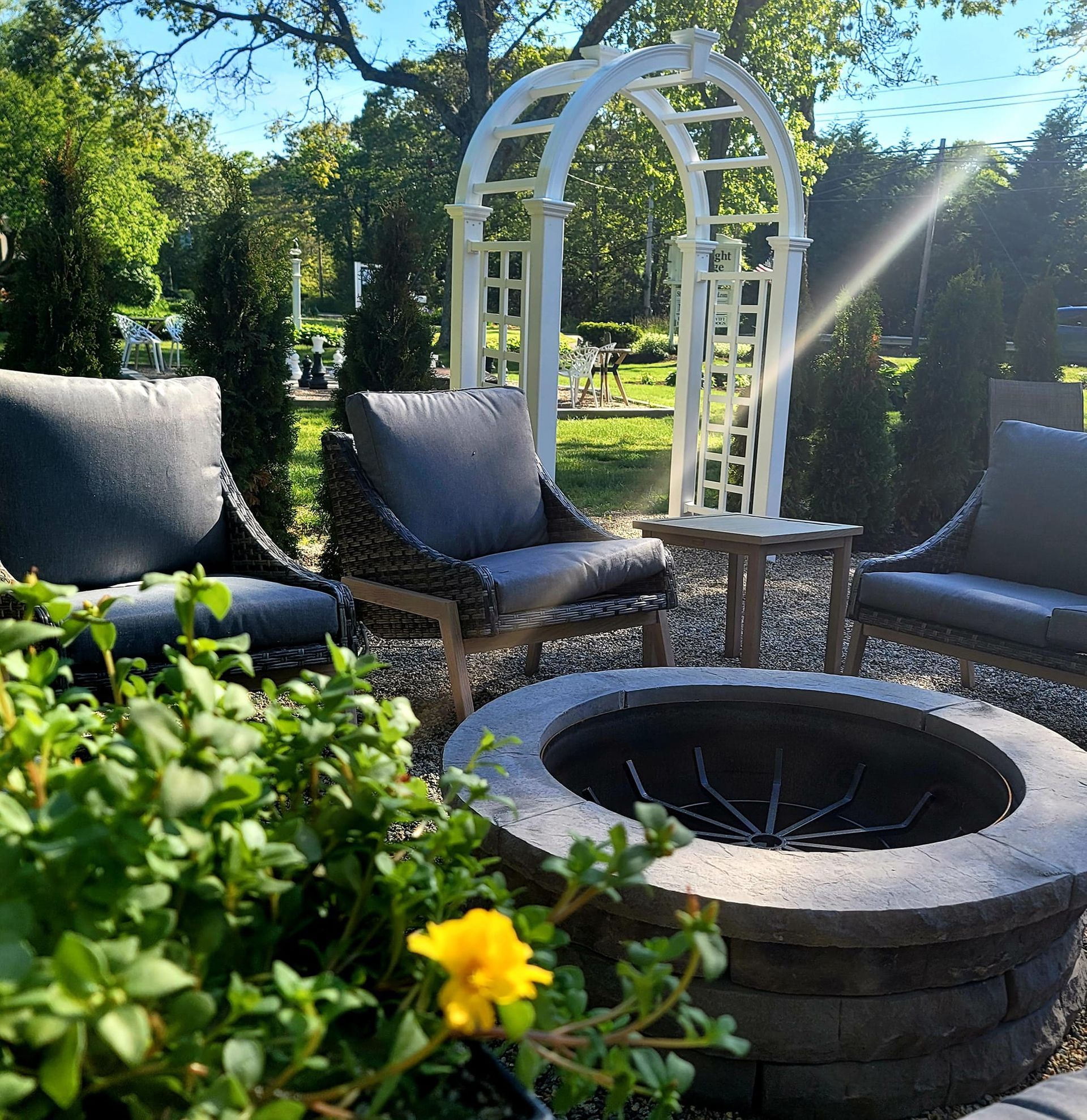 Outdoor seating area with fire pit, chairs, arbor, and greenery.