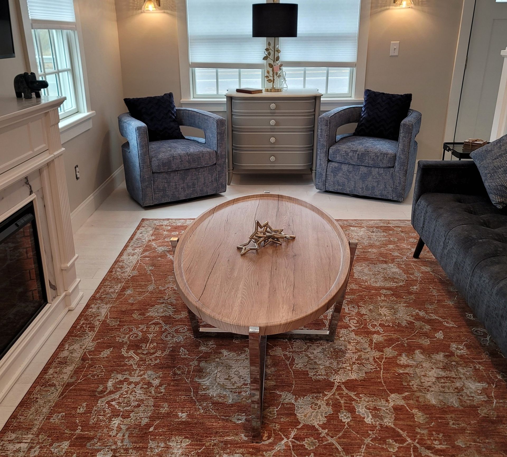 Living room: two blue patterned chairs, orange rug, round coffee table, fireplace.