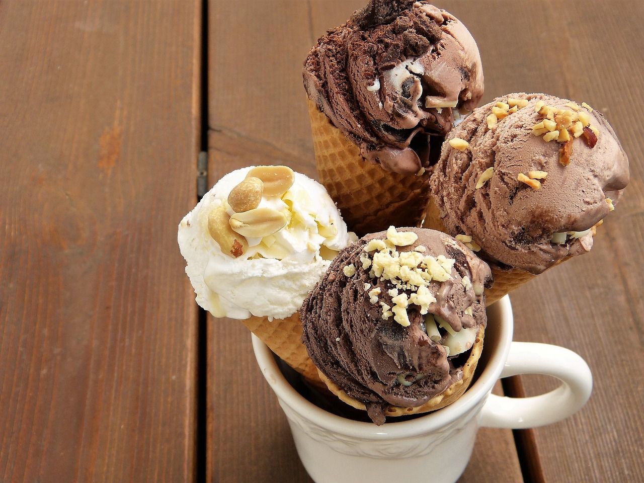 Ice cream cones in a white cup on a wooden table. Flavors include chocolate, vanilla, and hazelnut.