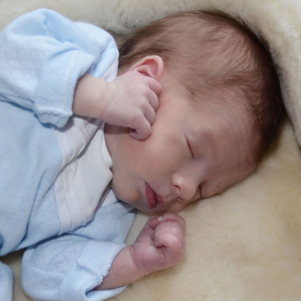 Een baby in een blauw pakje slaapt op een deken